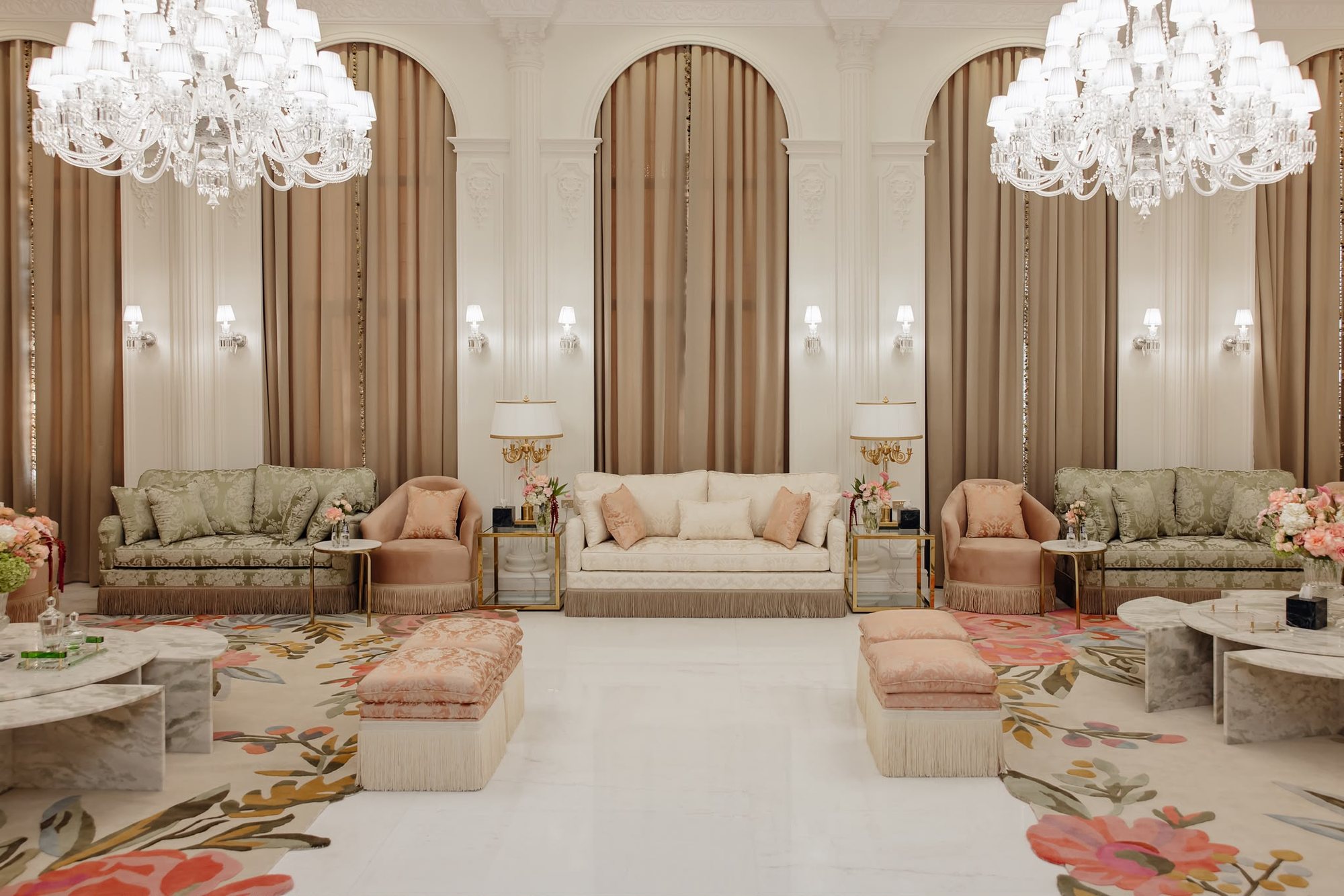 Wide real project room with arched wall details, chandeliers, cream seating, sage chairs, and blush ottomans