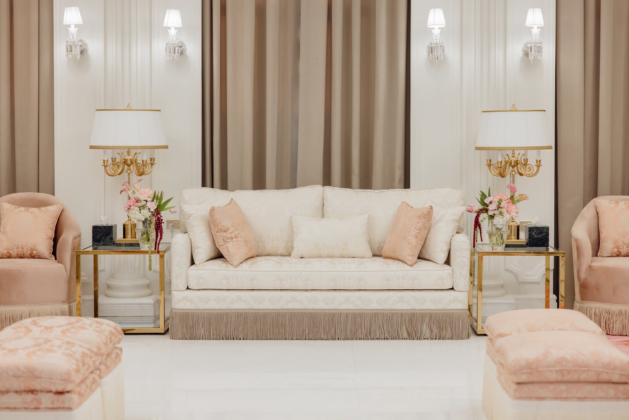 Real project lounge with cream sofa, blush seating, champagne side tables, taupe curtains, wall lights, and floral accents