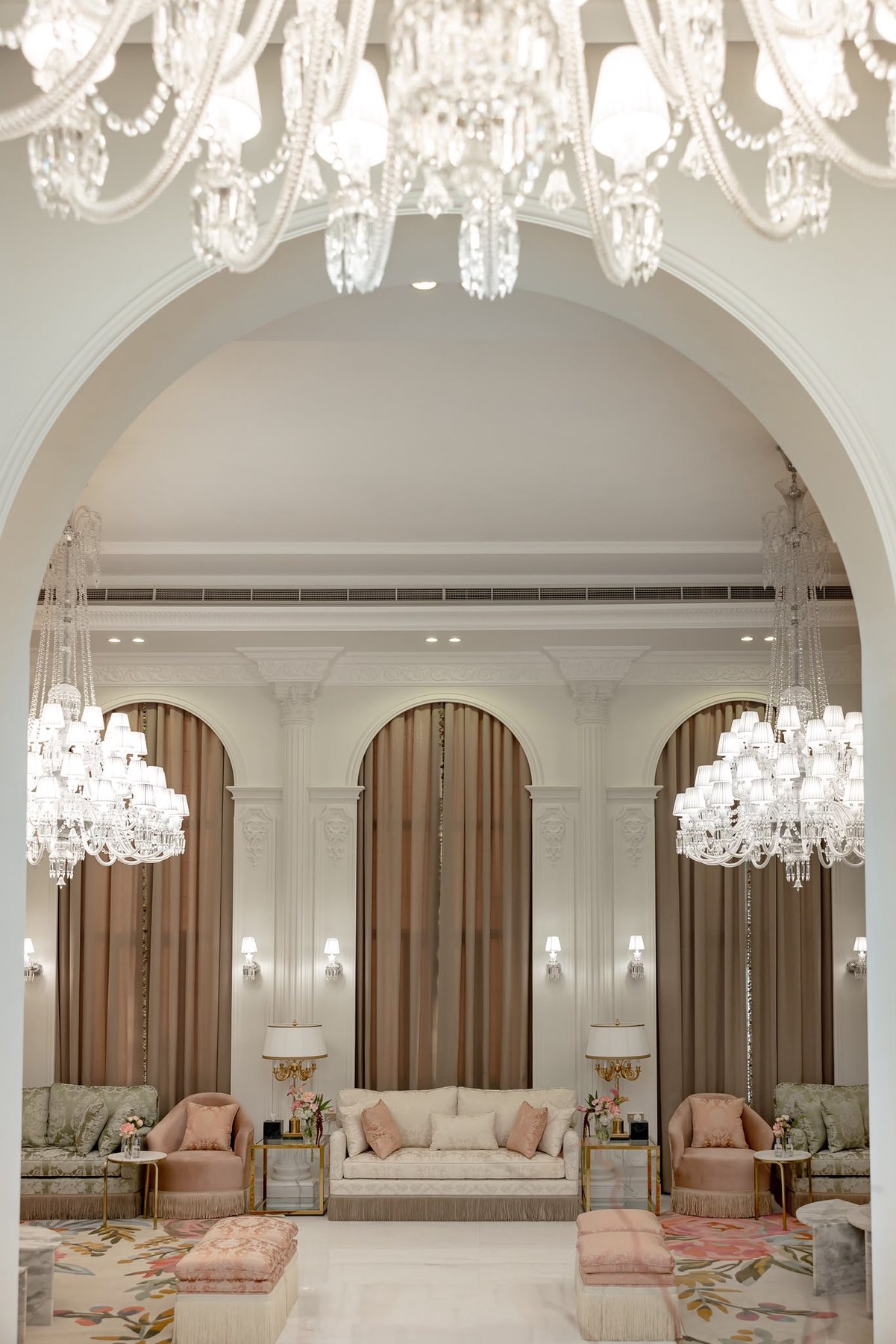 Real project view through an arch toward chandeliers, seating, taupe curtains, and marble table